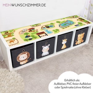 Può includere: Un mobile contenitore bianco con quattro scomparti, ciascuno con un contenitore in tessuto grigio scuro. I contenitori presentano illustrazioni di animali dei cartoni animati: un leone, una zebra, una giraffa e una tigre. La parte superiore è decorata con un design a tema zoo.