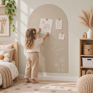 Op de afbeelding: Een beige boogvormig magnetisch wandbord met witte lijntekeningen van bloemen en een hart, met de Duitse tekst "Träum weiter kleine Entdeckerin" in het wit. Het bord bevat een regenboogtekening en een notitie met tekst.
