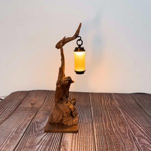 May include: A unique table lamp featuring a natural wood base and a branch-like structure. The lamp holds a cylindrical, ribbed glass shade that emits a warm, inviting glow. The lamp's design highlights the beauty of natural materials.