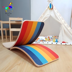 May include: A wooden rainbow rocker board with a rainbow design on the top and bottom. The board is curved and can be used for balance and coordination exercises.