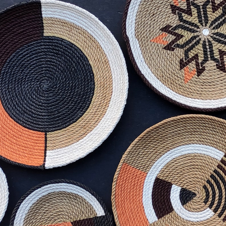 Puede incluir: Una colecci&oacute;n de cuencos decorativos de cuerda tejida en varios tama&ntilde;os y dise&ntilde;os. Los cuencos presentan una mezcla de colores, incluyendo negro, marr&oacute;n, naranja, beige y blanco. Algunos cuencos tienen patrones geom&eacute;tricos, otros dise&ntilde;os en espiral o radiales.