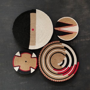 Peut inclure: Quatre décorations murales tissées en noir, blanc, rouge et marron. La plus grande pièce présente un motif rayé noir et blanc avec un point rouge au centre. Les trois autres pièces présentent une variété de motifs géométriques.