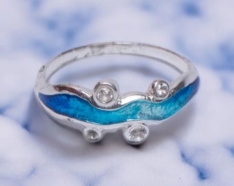 Könnte beinhalten: Ein silberner Ring mit einem blauen und türkisfarbenen Wellendesign aus Emaille und klaren Zirkonia-Steinen.