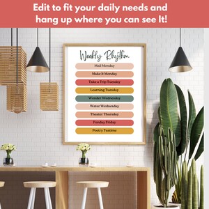 May include: A printable weekly schedule poster with the title "Weekly Rhythm" and a list of daily activities, such as "Mail Monday", "Make It Monday", "Take a Trip Tuesday", "Learning Tuesday", "Wonder Wednesday", "Water Wednesday", "Theater Thursday", "Funday Friday", and "Poetry Teatime". The poster is framed and hanging on a white brick wall in a room with plants and lamps.