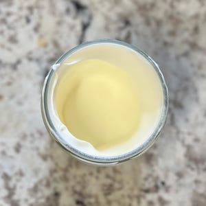 May include: A glass jar with a white lid, filled with a pale yellow substance. The jar is almost empty.