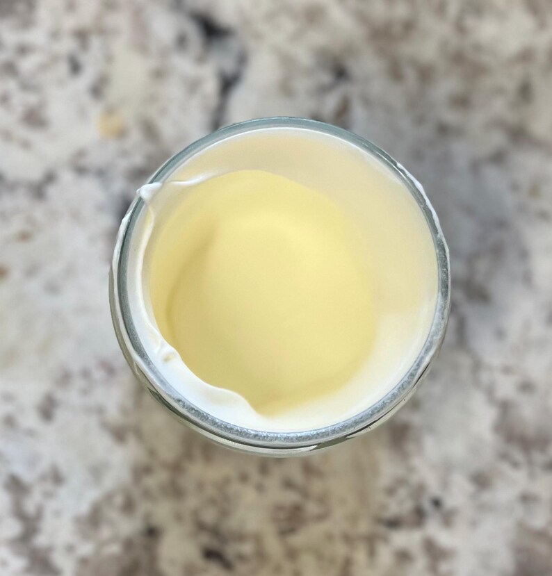 May include: A glass jar with a white lid, filled with a pale yellow substance. The jar is almost empty.