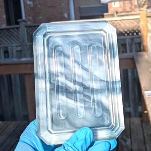 Puede incluir: Un jabonera de vidrio transparente con un diseño de mármol. La jabonera tiene tres crestas elevadas en la parte inferior.