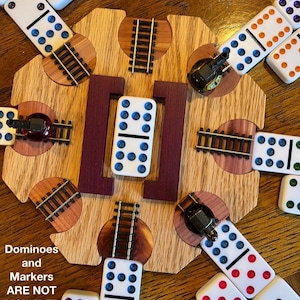 May include: A wooden dominoes game board with inlaid train tracks and a central purple accent. Dominoes with colored dots surround the board. Text reads "May be PERSONALIZED" and "Dominoes and Markers ARE NOT INCLUDED".
