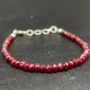 Puede incluir: Una pulsera de cuentas con pequeñas piedras preciosas facetadas de color rojo intenso. La pulsera está ensartada en un cordón flexible y se asegura con un cierre plateado. Las piedras son de tamaño uniforme y están muy juntas.