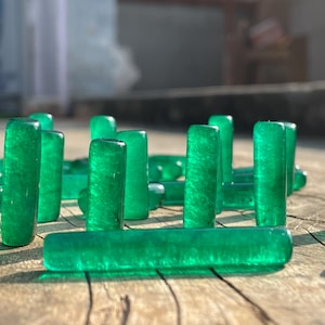 Op de afbeelding: Een verzameling groene glazen staven in verschillende lengtes, sommige staan ​​verticaal en andere liggen horizontaal op een houten oppervlak.