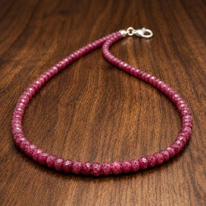 Puede incluir: Un collar compuesto por pequeñas cuentas redondas facetadas de color rosa intenso ensartadas. El hilo presenta un cierre de mosquetón de metal plateado en el extremo, lo que proporciona un cierre seguro para la disposición circular de las cuentas.