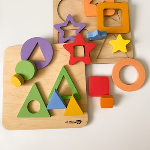 Könnte beinhalten: Ein Holzpuzzle-Set mit bunten Formen, darunter ein Stern, ein Kreis, ein Quadrat und ein Dreieck. Die Formen sind aus den Holzbrettern ausgeschnitten und können auf die Bretter gelegt werden. Das Puzzle-Set wird von der Firma "Wittlewood" hergestellt.