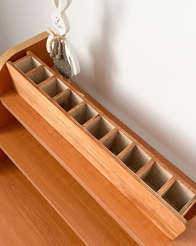 May include: A wooden organizer with multiple compartments, perfect for storing small items. The organizer is made of light brown wood and has a natural finish. It is sitting on a shelf made of the same wood.