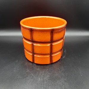 May include: Orange ceramic planter with a geometric design. The planter has a square pattern around the sides.