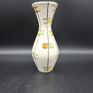 May include: A white ceramic vase with a geometric pattern in brown, orange, and green. The vase has a textured surface and a narrow neck.