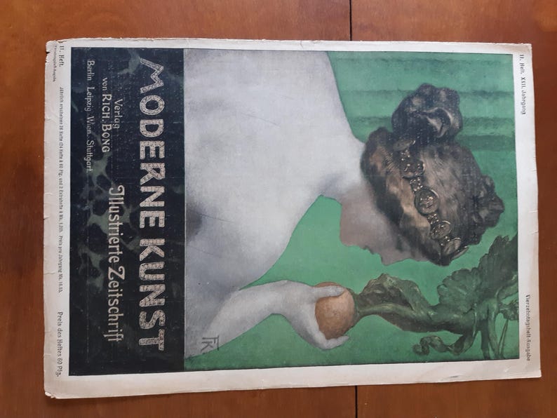 May include: A vintage magazine cover featuring a woman with a dark brown hat and a white dress. The magazine is titled "Moderne Kunst" and is an illustrated journal. The woman is holding a turnip in her hand.