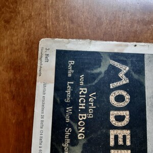 May include: A black and white magazine cover with the word "MODE" in large, gold letters. The magazine is published by Verlag von Rich. Bong and is from Berlin, Leipzig, Wien, and Stuttgart. The cover states that it is the 3rd issue and is a bi-weekly publication.