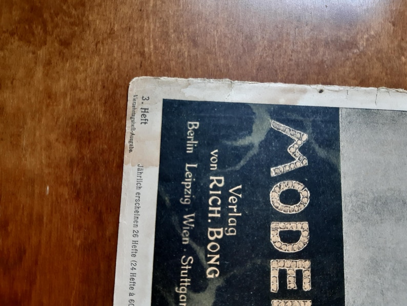 May include: A black and white magazine cover with the word "MODE" in large, gold letters. The magazine is published by Verlag von Rich. Bong and is from Berlin, Leipzig, Wien, and Stuttgart. The cover states that it is the 3rd issue and is a bi-weekly publication.