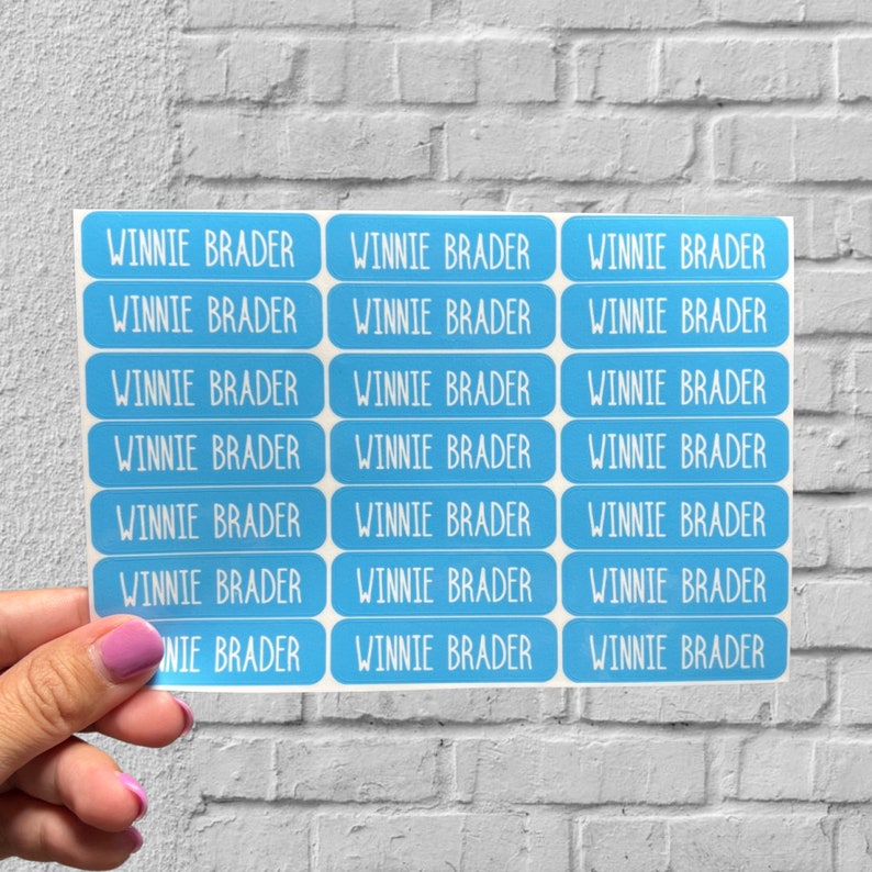 May include: A sheet of blue rectangular stickers with the name "WINNIE BRADER" printed in white on each sticker.