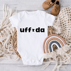 May include: White baby onesie with black text that says "uff da" and a small outline of the state of Minnesota.
