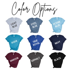 Op de afbeelding: Een selectie T-shirts in verschillende kleuren, waaronder lichtblauw, staalblauw, aqua, oceaanblauw, koninklijkblauw, marineblauw, bordeauxrood, asfalt en zwart. Elk shirt heeft een wit tekstlabel met de kleurnaam.