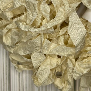 May include: A close-up of a pile of ivory silk ribbon. The ribbon is soft and delicate, with a subtle sheen.