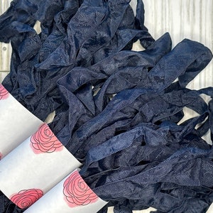 May include: A bundle of navy blue fabric ribbon wrapped around three white paper tubes with pink floral designs.