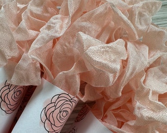 May include: A close-up of a pile of pale pink satin ribbon with a white label that says "art & effort" and has a black and pink rose design.