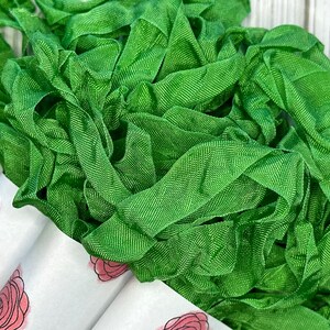 May include: A pile of green silk ribbon, perfect for crafting and decorating. The ribbon is soft and has a subtle sheen.