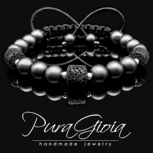 May include: Black beaded bracelet with a black lava rock bead and silver accents. The bracelet is tied with a black cord and has a reflection on a black surface. The text "Pura Gioia handmade jewelry" is visible below the bracelet.