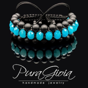 May include: A black and turquoise beaded bracelet with a black cord. The bracelet is made with round beads and features a knot design. The brand name "Pura Gioia handmade jewellery" is visible at the bottom of the image.