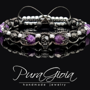 Puede incluir: Un brazalete de cuentas negras y moradas con un dije de calavera y piedras de amatista. El brazalete está hecho con cuentas de ónix negro y un dije de calavera plateada. El brazalete está atado con un cordón negro y tiene un cierre plateado.
