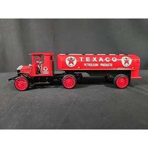 May include: A red and black Texaco tanker truck toy. The truck has red wheels and a red cab. The tanker trailer is red with the Texaco logo and "Petroleum Products" printed on the side. The truck has "The Texas Company" printed on the side.