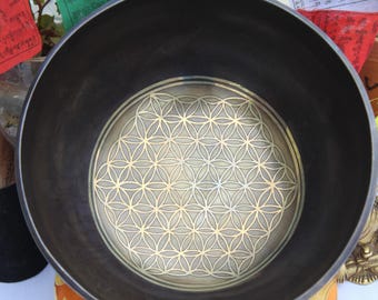 Può includere: Una ciotola cantate grigio scuro con un design a fiore della vita in oro. La ciotola è in metallo e ha una superficie liscia e lucida.