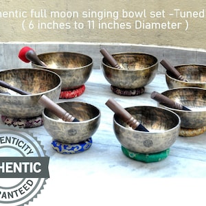 May include: Set of seven antique-looking singing bowls with mallets, ranging in size from 6 to 11 inches in diameter. The bowls are arranged on a light-colored surface. The bowls are tuned to the notes A through G.  "Authenticity Guaranteed" is printed on a circular sticker.