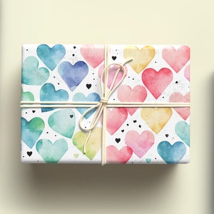 May include: Two rolls of wrapping paper. One roll features a pattern of colorful watercolor hearts on a white background. The other roll features a pattern of colorful flowers and leaves on a dark blue background.