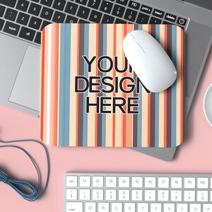 May include: A striped mouse mat with the text "YOUR DESIGN HERE" on it. A white wireless mouse is on the mouse mat. A laptop, a keyboard, a cup of coffee, and a pair of blue headphones are also in the image.