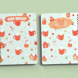 Pode incluir: Um caderno espiral azul e branco com um design temático de Natal. A capa apresenta um padrão de canecas vermelhas com marshmallows, casas de gengibre e flocos de neve. O texto "BOOK MOCKUP" está impresso na capa.