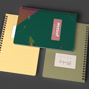 May include: Three spiral bound notebooks with different covers. The top notebook has a green cover with geometric shapes and the text "MOCKUP BOOK COVER". The middle notebook has a yellow cover with a grid pattern. The bottom notebook has a green cover with the text "MOCKUP BOOK COVER".