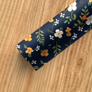 May include: A roll of blue wrapping paper with a floral pattern featuring white and yellow flowers, green leaves, and orange accents.