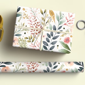 Op de afbeelding: Een cadeauverpakking verpakt in bloemen aquarel papier met een bijpassende rol papier. Het ontwerp toont roze bloemen, groene bladeren en bruine stelen op een witte achtergrond. Een gele meetlint en een zilveren schaar staan ook in de afbeelding.
