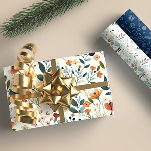 May include: A gift wrapped in white floral patterned paper with a gold ribbon and bow. Two rolls of wrapping paper are visible in the background, one with a blue floral pattern and the other with a blue pattern of scientific symbols.