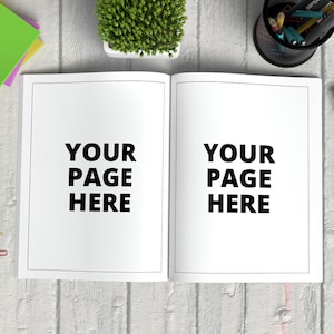 May include: A white open notebook with the text "YOUR PAGE HERE" on each page. The notebook is on a white wooden surface with a variety of office supplies, including a stapler, paper clips, sticky notes, a pencil holder, and a potted plant.