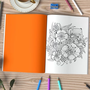 May include: An open coloring book with an intricate black and white floral design on one page. The other page is blank and orange. The book is surrounded by pencils, erasers, and a rose.
