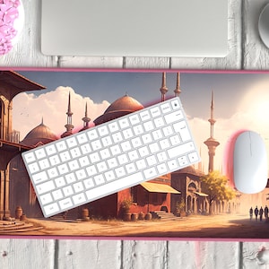 Könnte beinhalten: Eine rosa und weiße Mausmatte mit einer Stadtbild-Illustration, die Gebäude mit Minaretten und einen Sonnenuntergangshimmel zeigt. Eine weiße kabellose Tastatur und Maus befinden sich auf der Matte.