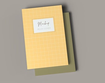 以下が含まれることがあります： グリッドパターンと白い長方形に「Mockup Book Cover」というテキストが書かれた黄色の本の表紙のモックアップです。