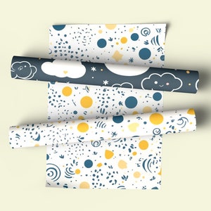 Puede incluir: Tres rollos de papel de regalo blanco con diferentes patrones. Los patrones incluyen círculos amarillos y azules, estrellas, nubes y formas abstractas.