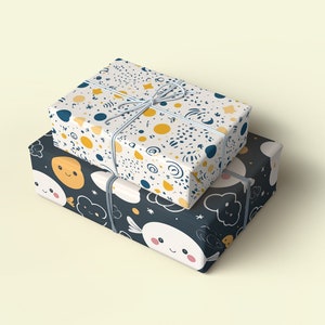 May include: Two gift boxes wrapped in colorful patterned paper. The top box is white with yellow, blue, and black abstract shapes. The bottom box is black with white clouds, stars, and yellow smiley faces.