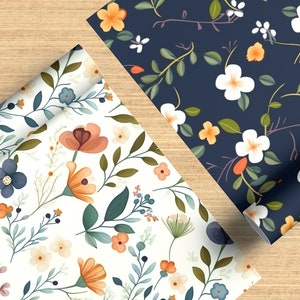 Puede incluir: Dos rollos de papel de regalo con estampado floral. Un rollo tiene un fondo blanco con flores naranjas, azules y marrones. El otro rollo tiene un fondo azul oscuro con flores blancas y amarillas.