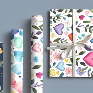 May include: Three rolls of wrapping paper with different floral and heart patterns. The paper is white with colorful watercolor hearts, flowers, and leaves. The rolls are on a light blue background.